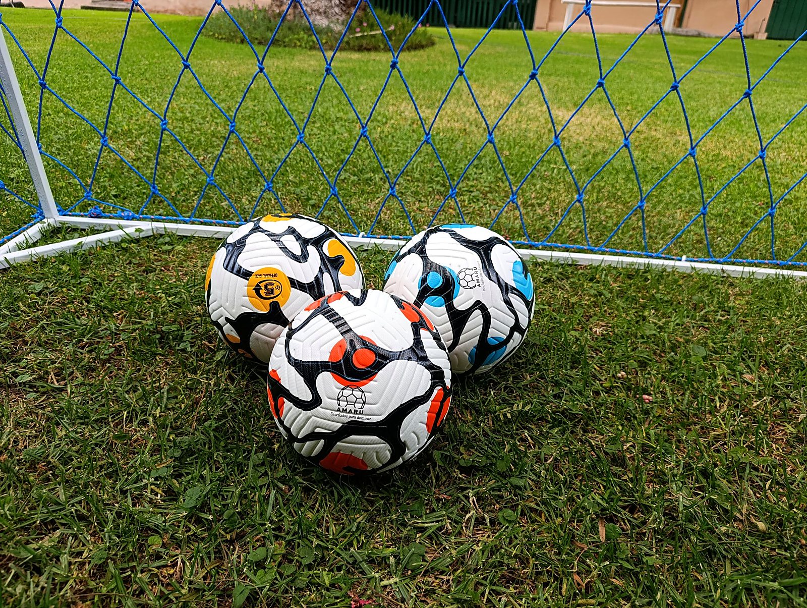 Tres balones AMARU frente a un arco con red azul